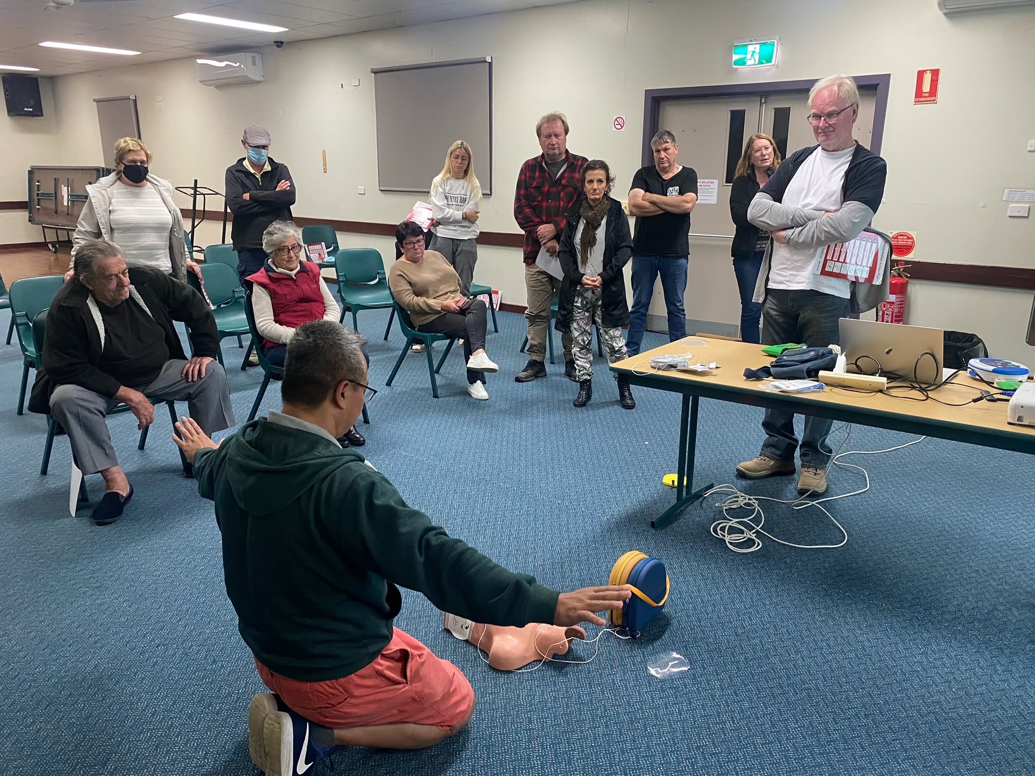An instructor demonstrating an AED with a training manikin to community members